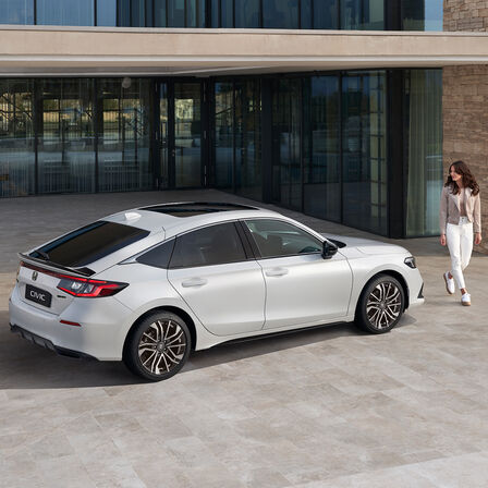 Žena přicházející k zaparkovanému vozu Honda Civic e:HEV