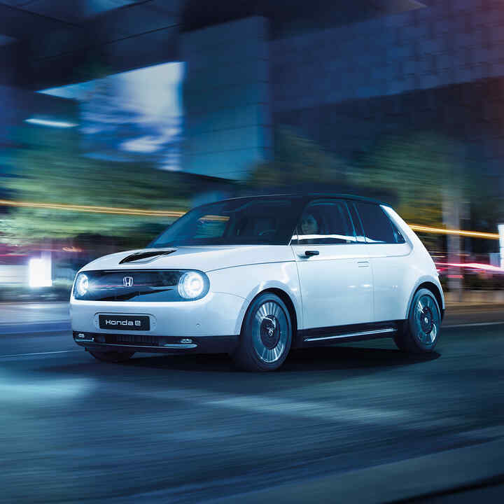 Tříčtvrtinový pohled zepředu na model Honda e při jízdě městem.