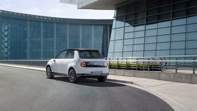 Zadní tříčtvrtinový pohled na model Honda e se skleněnými budovami v pozadí
